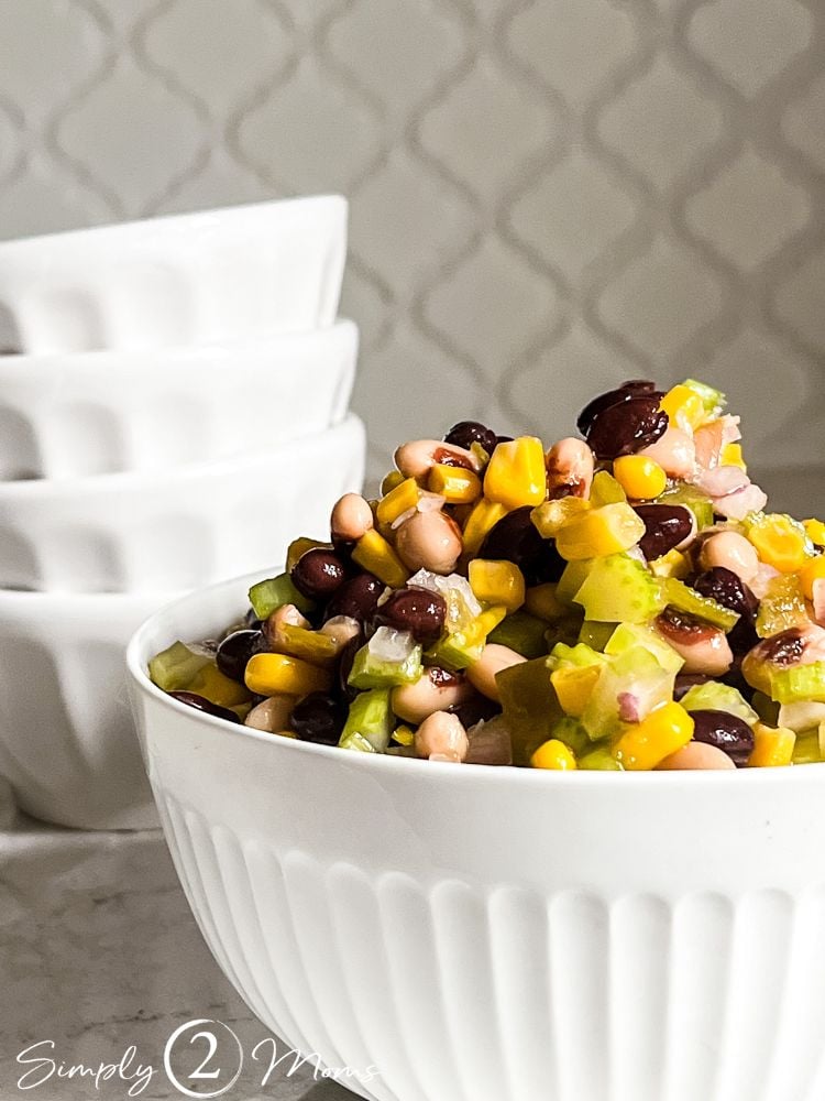Large white bowl containing bean, corn, and celery dip with 4 small serving bowls behind it.