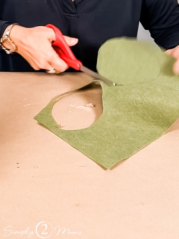 Woman using scissors to cut out circles of green felt to be used for the base of a DIY christmas tree decoaration