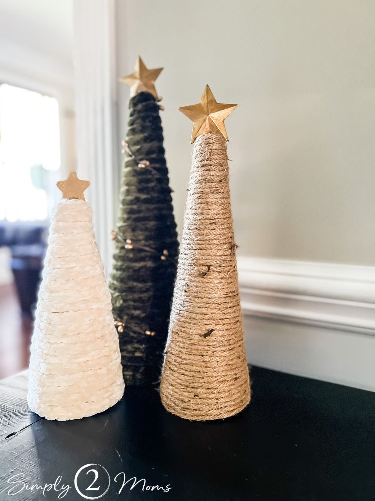 Three DIY christmas tree decor pieces made by wrapping styrofoam cones in chunky yarn then topped with gold stars.