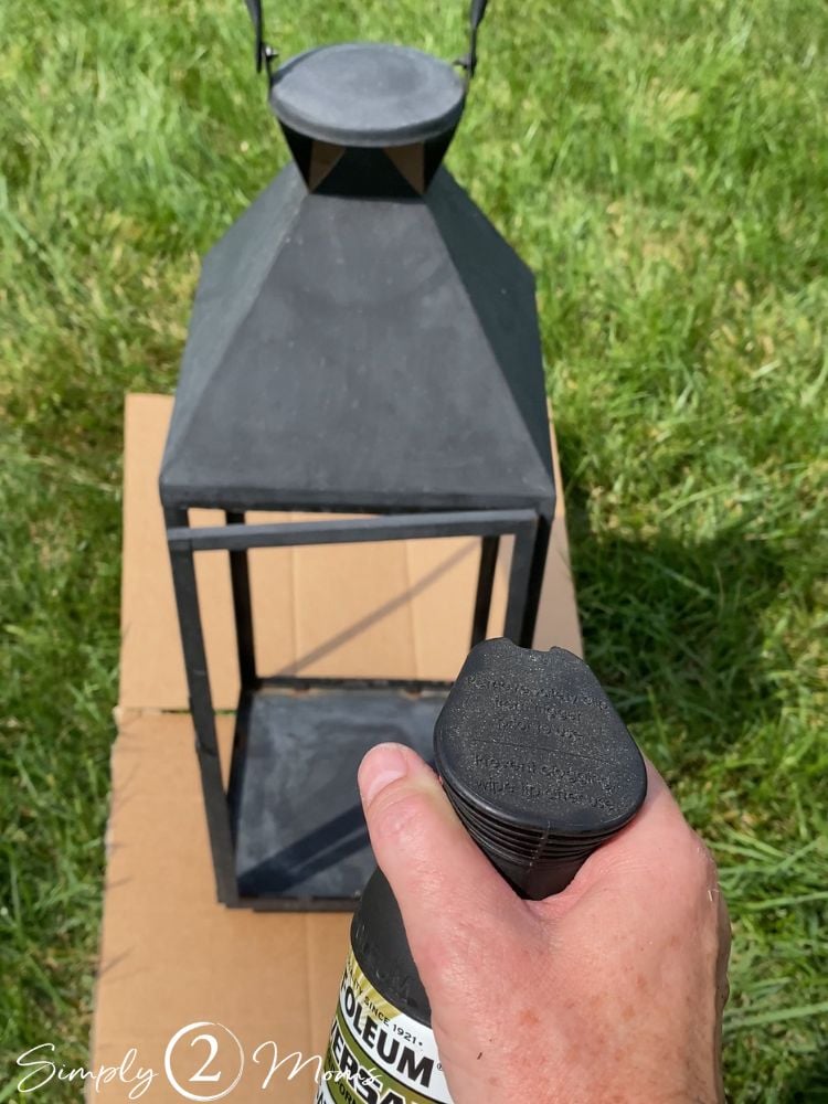 Person holding can of black spray paint up to an old and broken outdoor lantern to refurbish it
