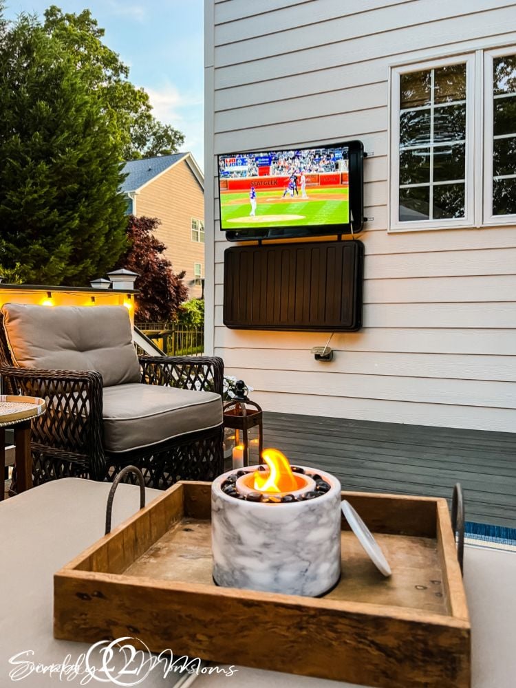 Outdoor TV with baseball game playing and a mini firepit on wooden tray on coffee table