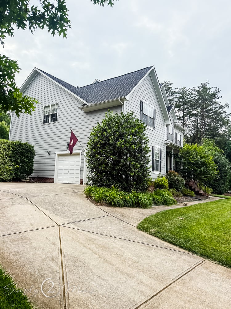 Pull back before photo of gray farmhouse with builder basic garage doors.