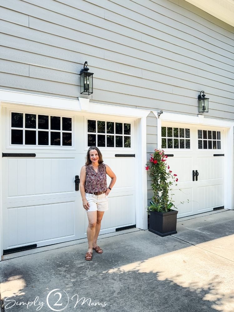 Woman standing in front of a 2 car garage with Churchill style garage doors with window panels and iron hardware.