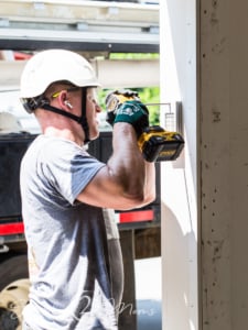 Installer wearing a hard hat and protective gear using a Dewalt driver to install a garage door keypad.