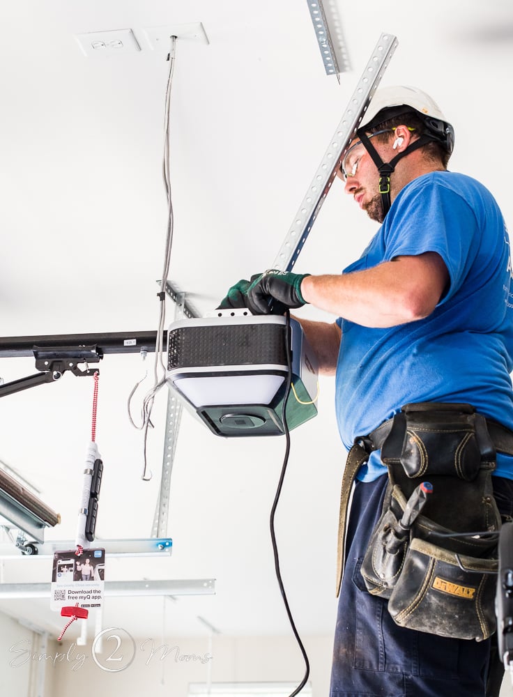 Man wearing a helmet and safety goggles installing a garage door lift system.