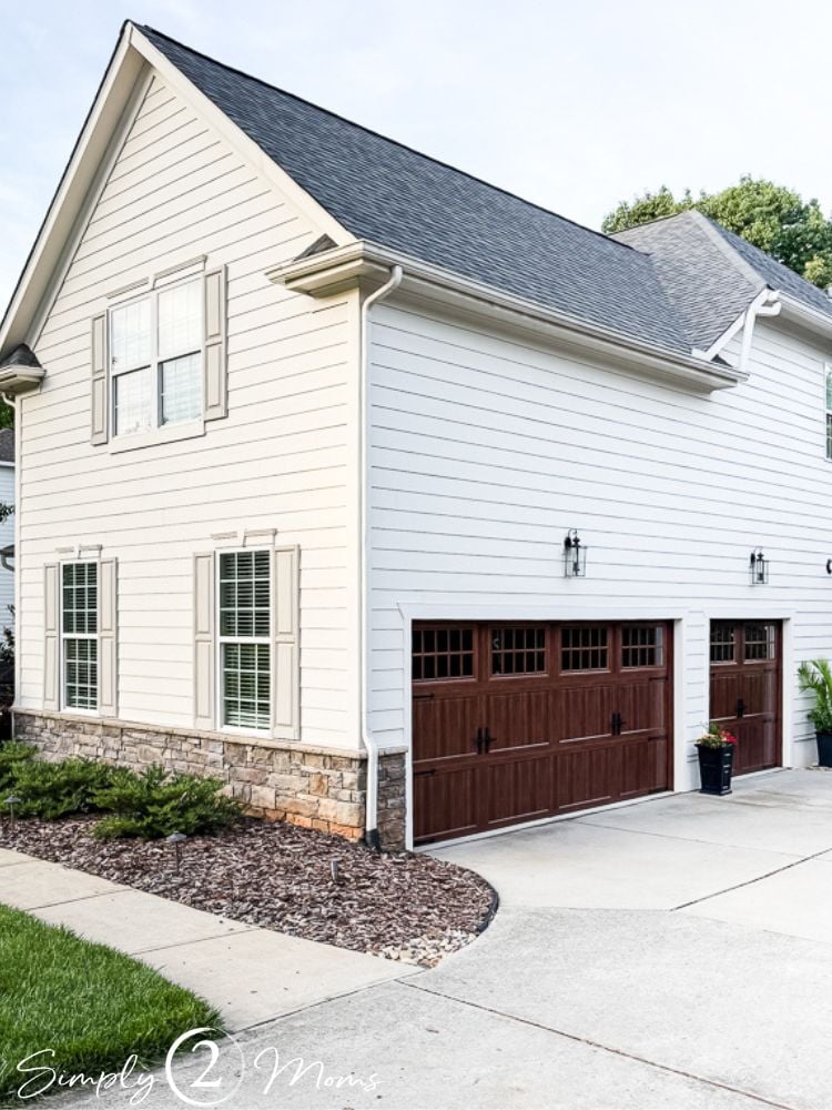 Pull back view of a classic home with a stone foundation and faux wood garage doors.