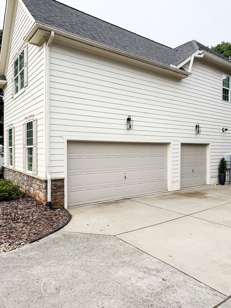Pull back view of a classic Shoji white house with stone foundation and Anew Gray garage doors.