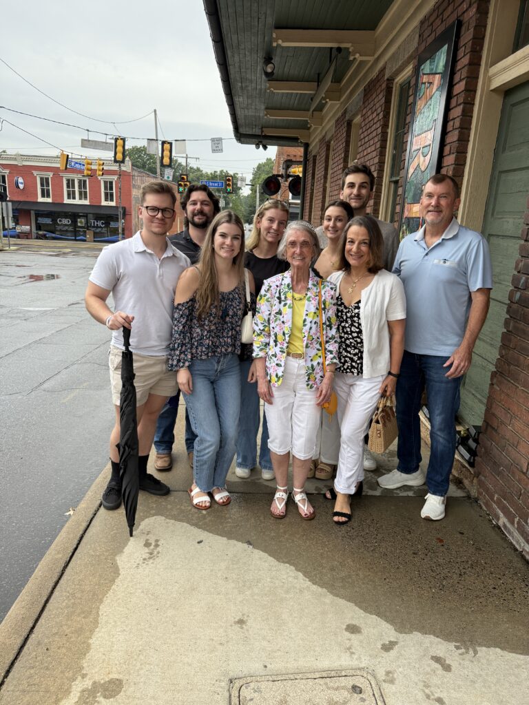 Large family group smiling together on a sidewalk after a birthday dinner outing, celebrating milestones with young adult children and grandparents.