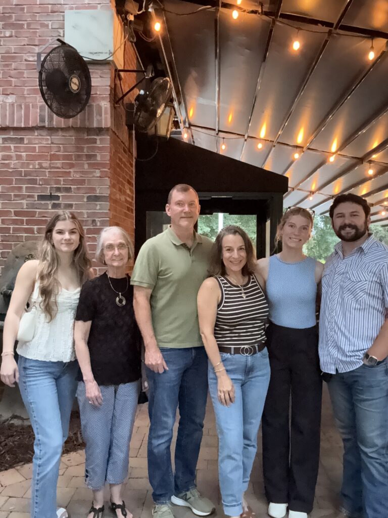 Family group photo at a restaurant under string lights, enjoying a birthday dinner night out with young adult kids and extended family.