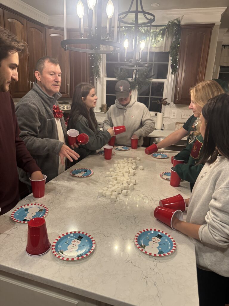 Family gathered around the kitchen island playing a fun holiday cup and marshmallow game on Christmas game night.