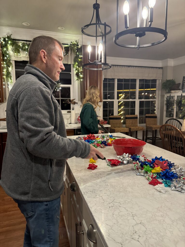 Father and daughter playing a Christmas party game with colorful bows spread across the counter during holiday family fun.