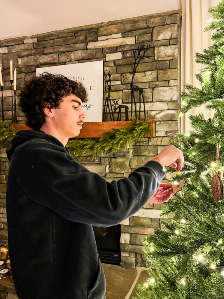 Teen decorating the family Christmas tree with ornaments, continuing holiday traditions at home.