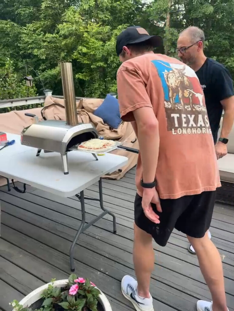 Father and son cooking homemade pizza together using an outdoor pizza oven during family pizza night.
