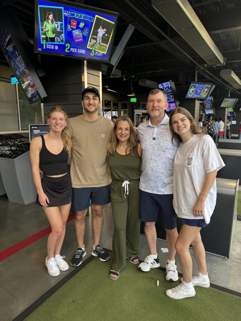 Family posing together at Top Golf, enjoying a casual game night of golf and fun with young adult kids.