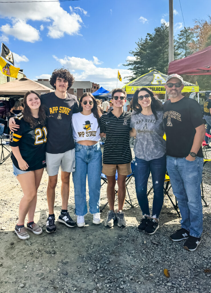 Family smiling together at an Appalachian State University tailgate, wearing team gear and enjoying a college football game day tradition.