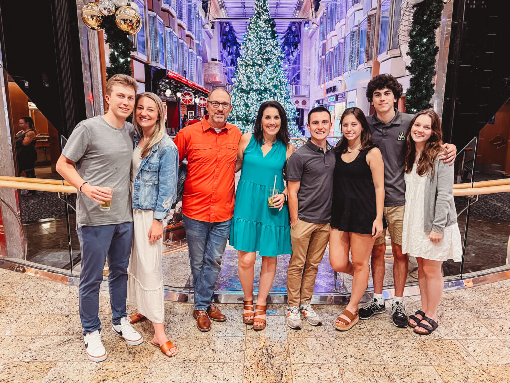 Family group dressed up on a cruise ship at Christmas, standing in front of a decorated tree and celebrating the holiday together.