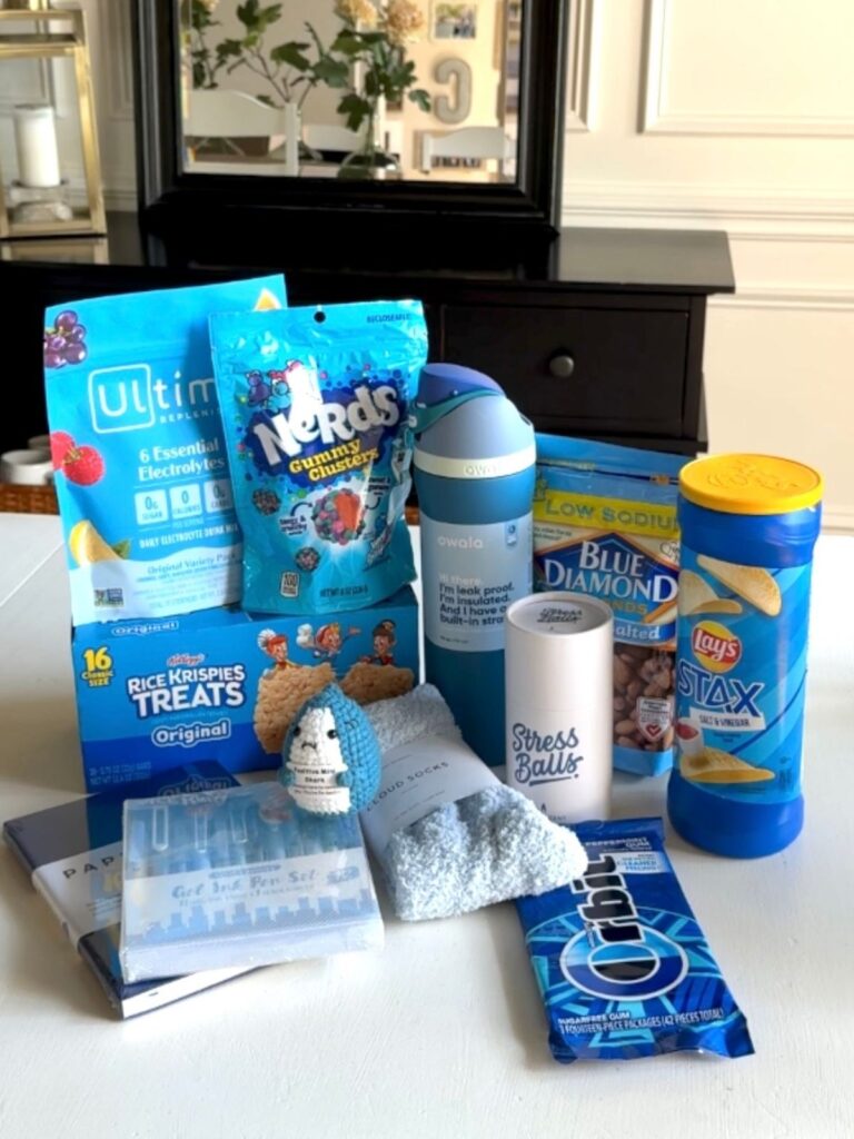 Blue-themed college care package items including snacks, water bottle, cozy socks, stress relief gift, and stationery laid out on a table