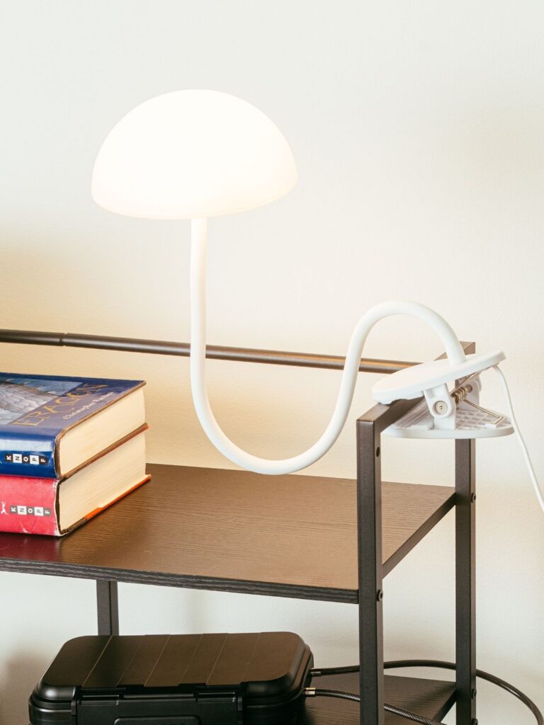 White desk lamp clipped to wooden desk shelf with books and lock box below