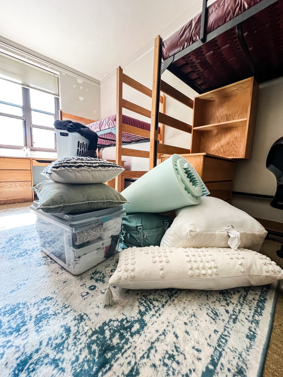 Dorm decor items including throw pillows and a mattress topper placed on a rug before packing.