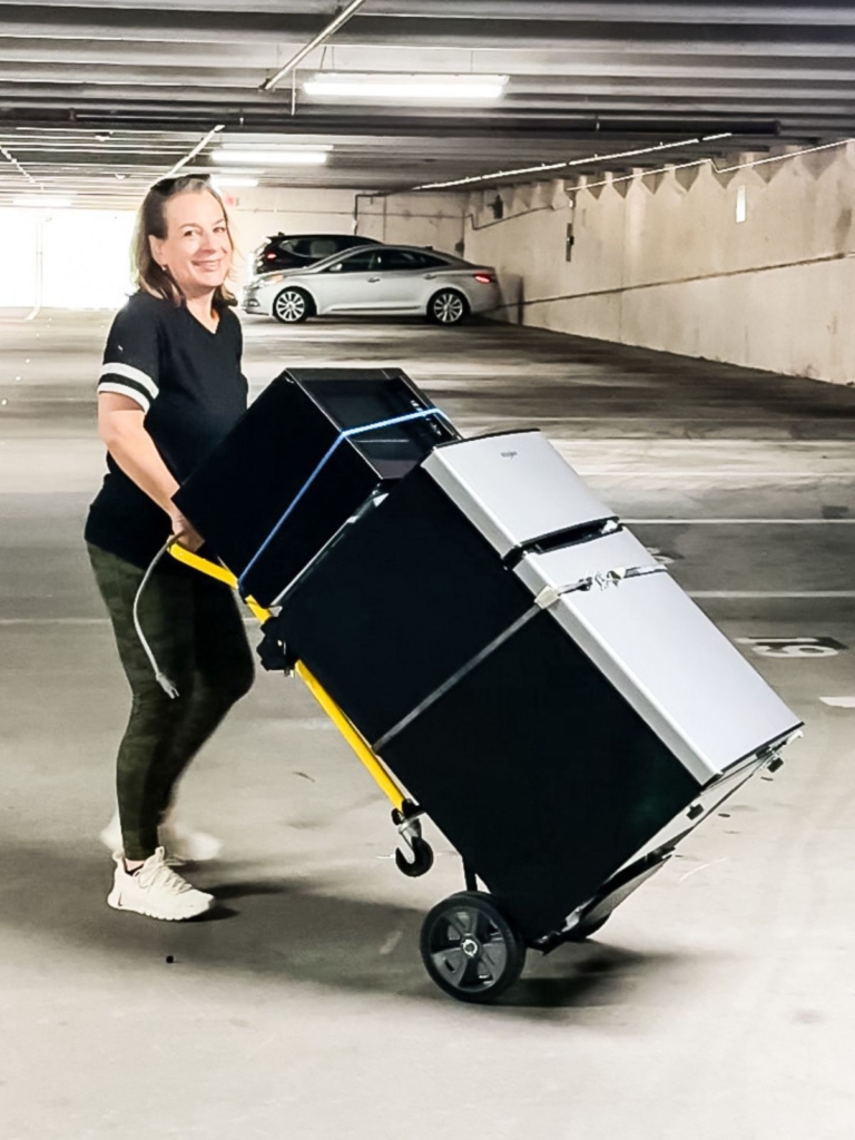 Mom using a hand truck to move a mini fridge and microwave out of a dorm room.