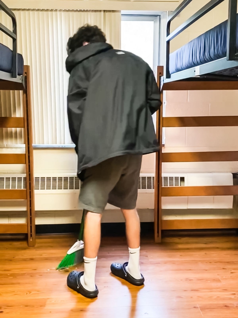 College student sweeping the dorm room floor while cleaning the room before checkout.