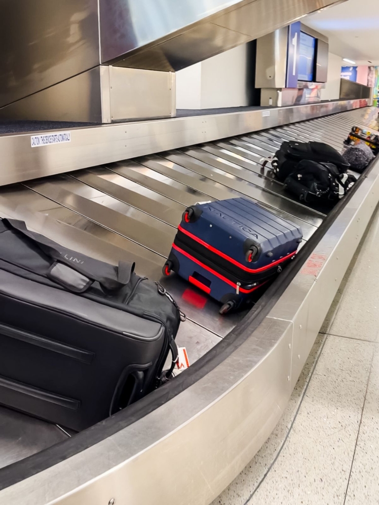 Several suitcases, including a black and a dark blue one with red accents, move along an airport baggage claim carousel. The area appears clean and bright.
